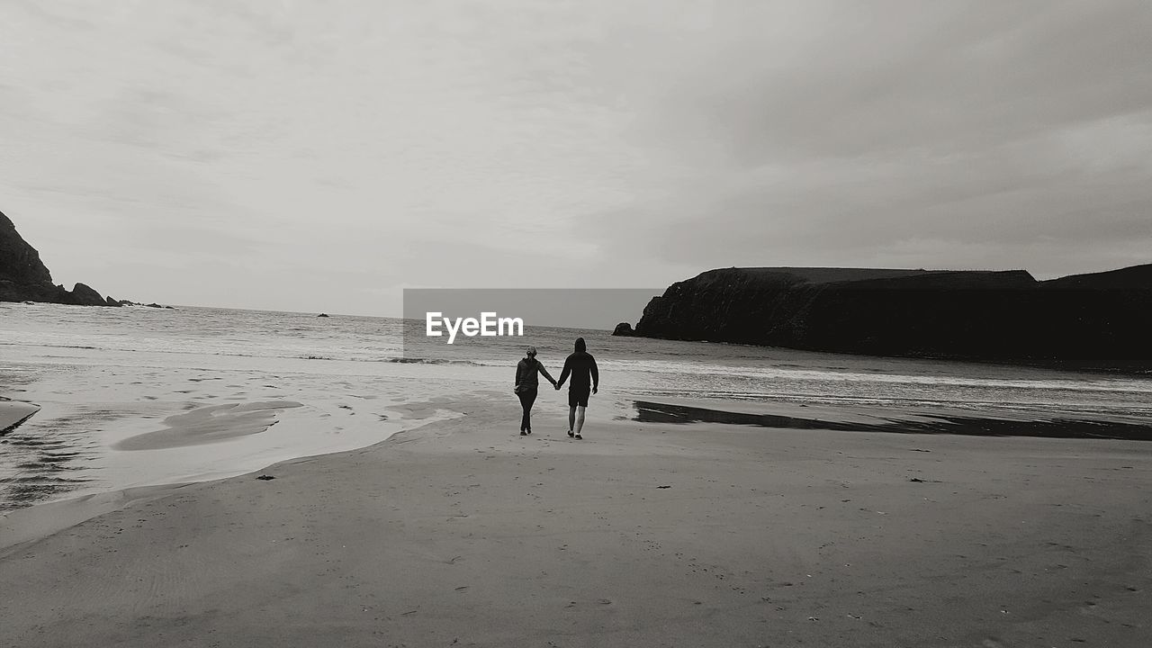 PEOPLE STANDING ON BEACH AGAINST SKY