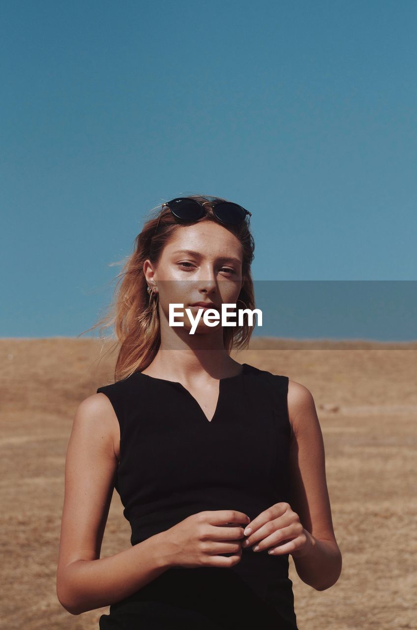 Portrait of beautiful young woman standing in desert against clear blue sky