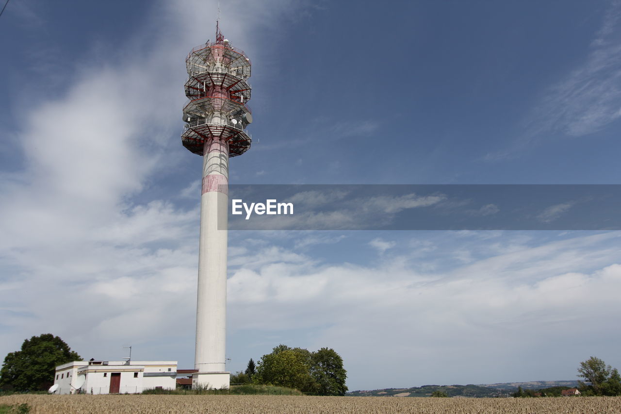 Low angle view of communications tower on field against cloudy sky