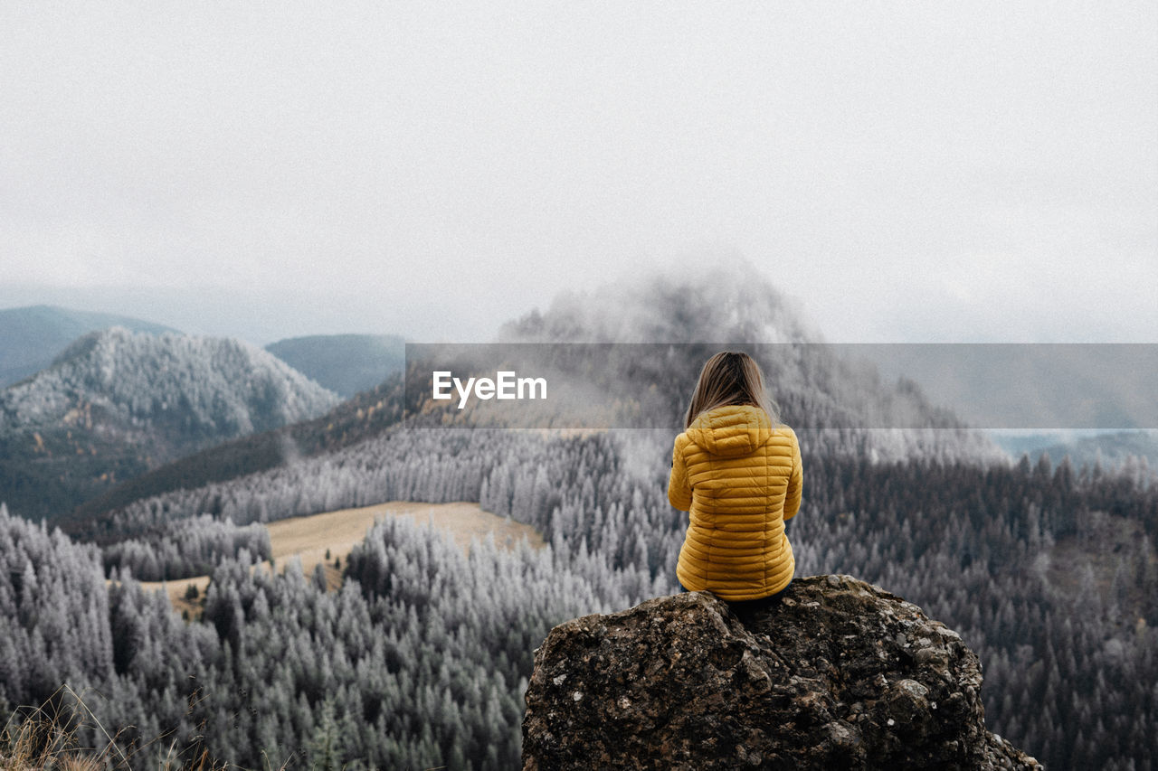 Young girl sitting on a rock with yellow jacket in the nature