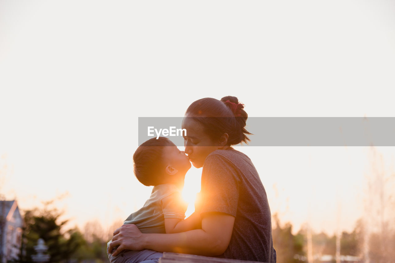 Mother and son kissing against sky during sunset