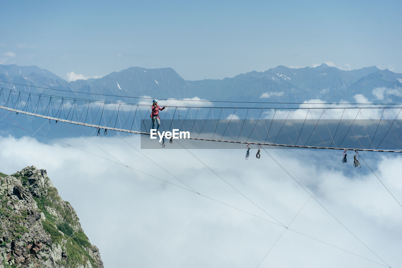 A person walks on a suspended rope bridge in the clouds. extreme attraction.