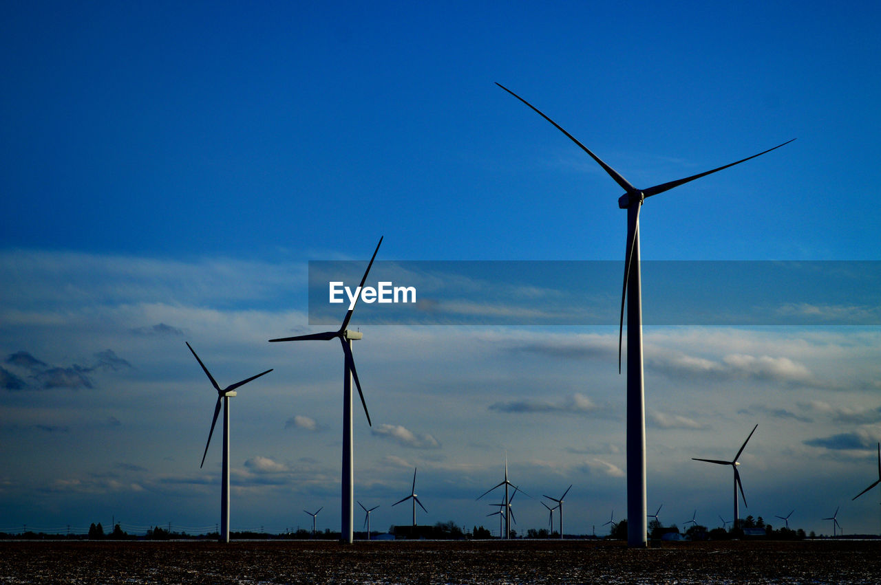 Low angle view of wind turbines on field