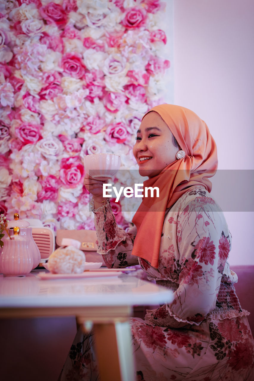 YOUNG WOMAN WITH PINK FLOWER ON TABLE