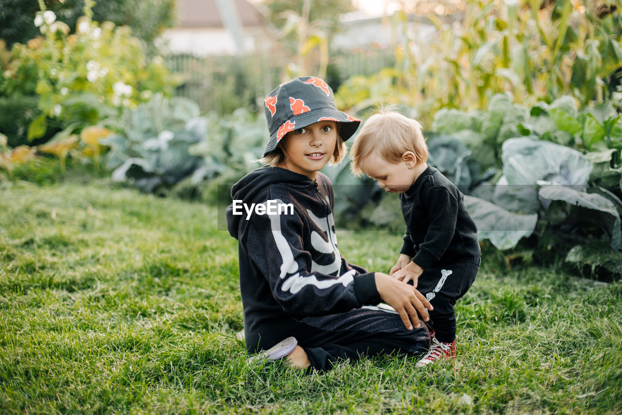 A happy blond boy and his sister in carnival skeleton costumes are playing in the garden