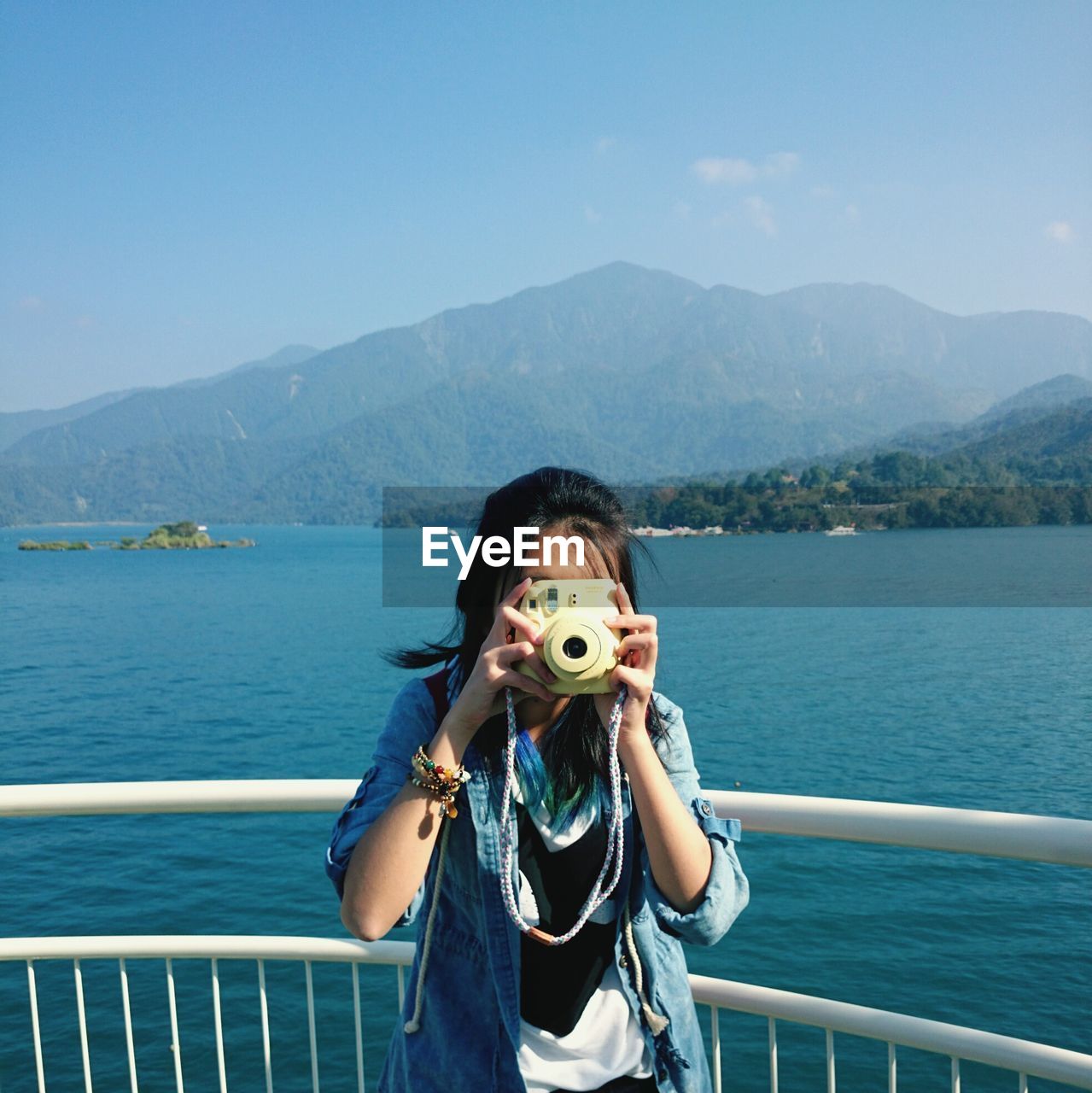 Woman photographing with instant camera while standing against sun moon lake
