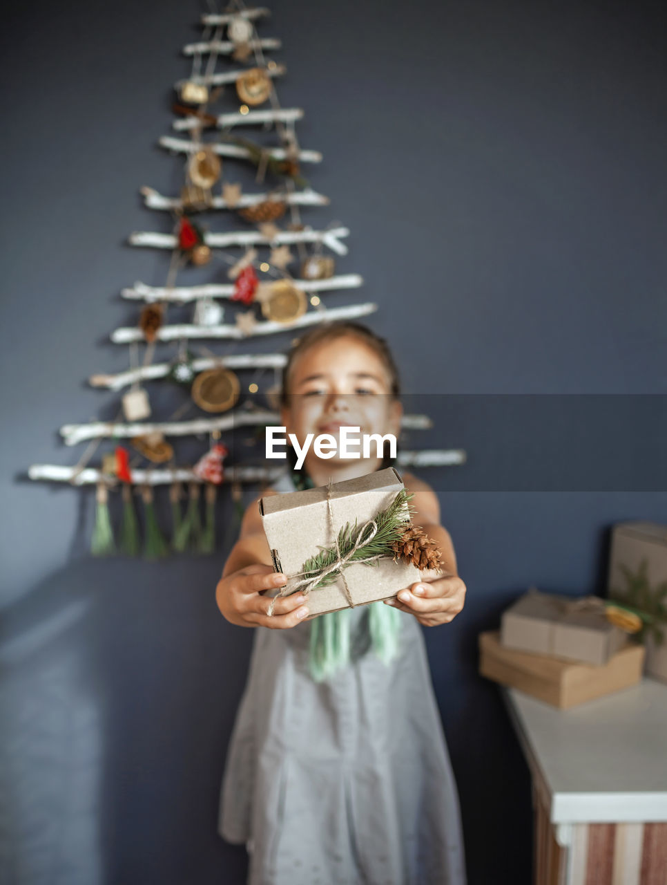 Portrait of smiling girl holding gift against christmas tree hanging on wall