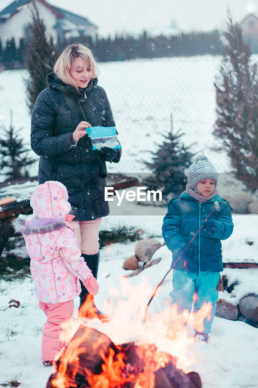 Mother with children standing on snow covered field at campfire