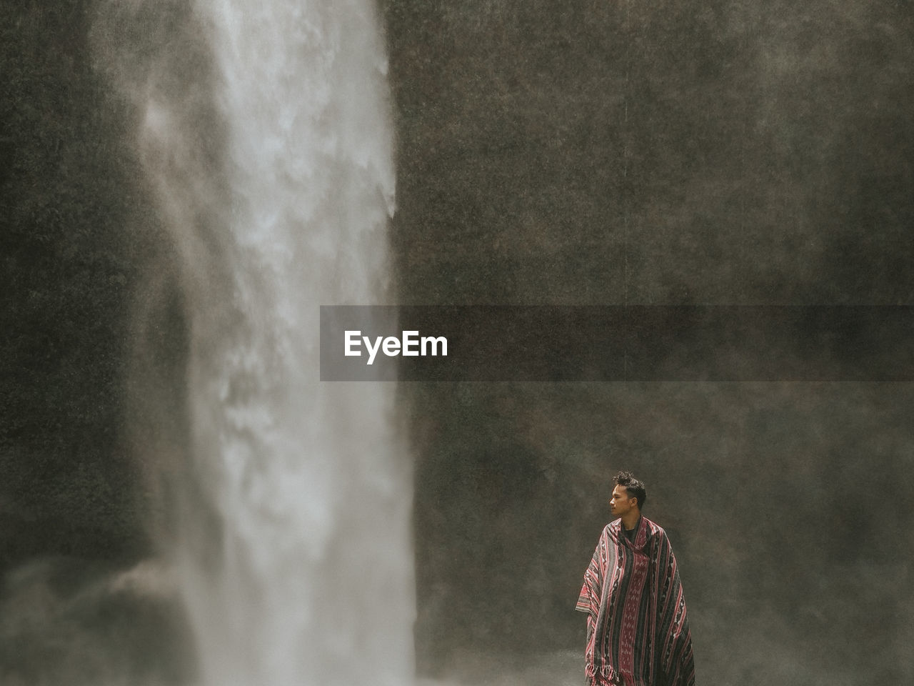 Man standing against waterfall falling from mountain