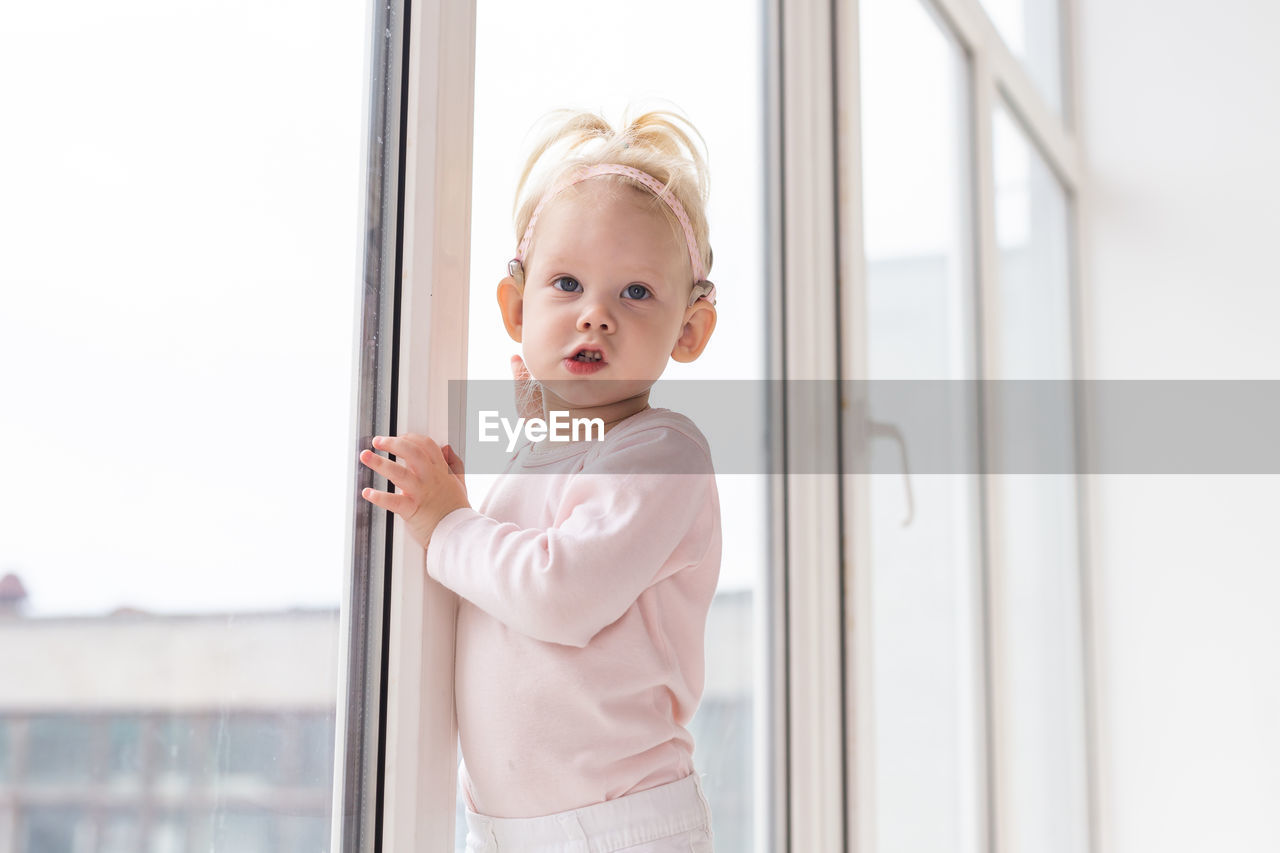 portrait of cute girl standing against window