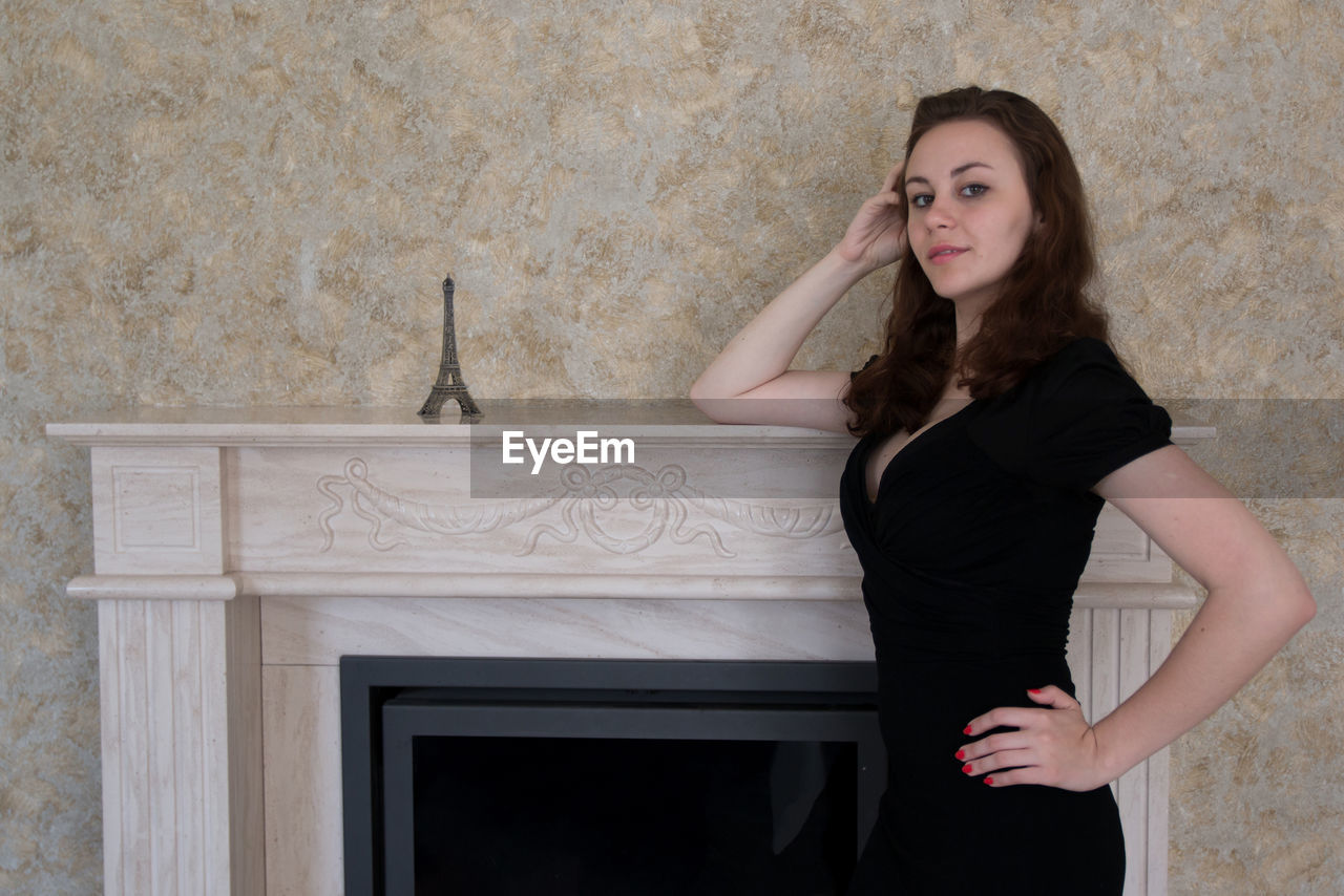 Portrait of young woman posing by eiffel tower replica on fireplace mantel at home