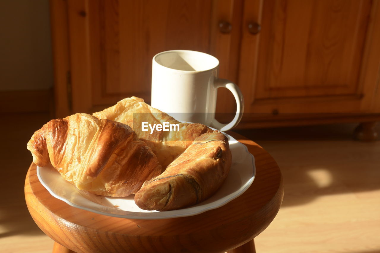 Close-up of croissant and coffee on stool at home