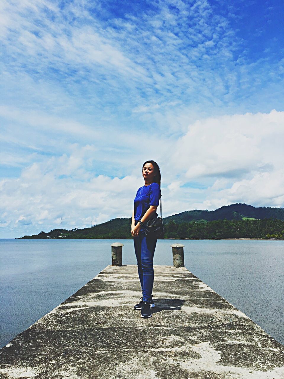 FULL LENGTH OF YOUNG WOMAN STANDING BY LAKE AGAINST SKY