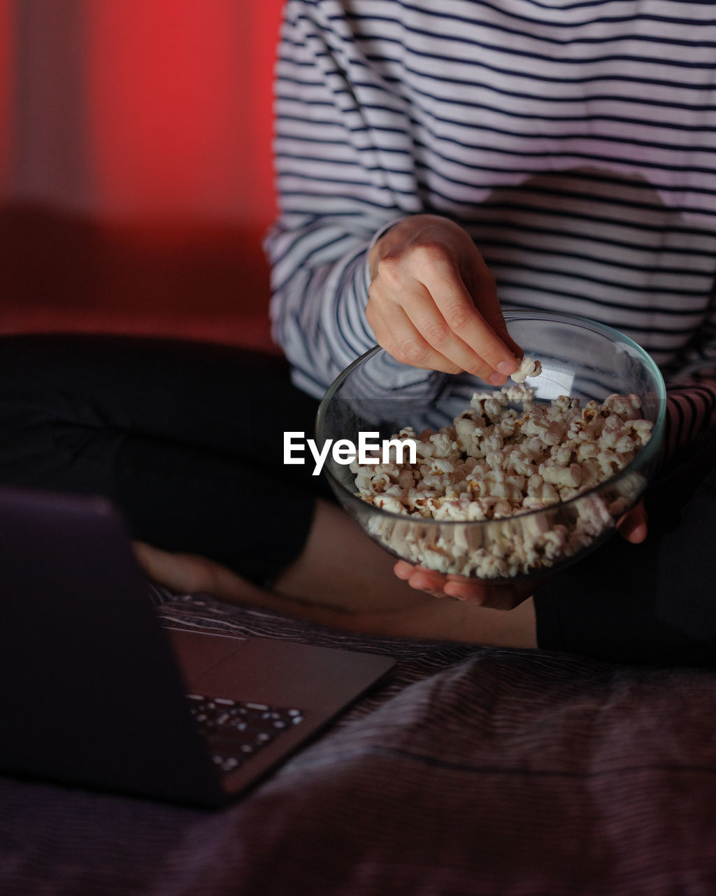 Woman in a striped sweatshirt and hat eats popcorn and watches a movie on tv or a tv series at