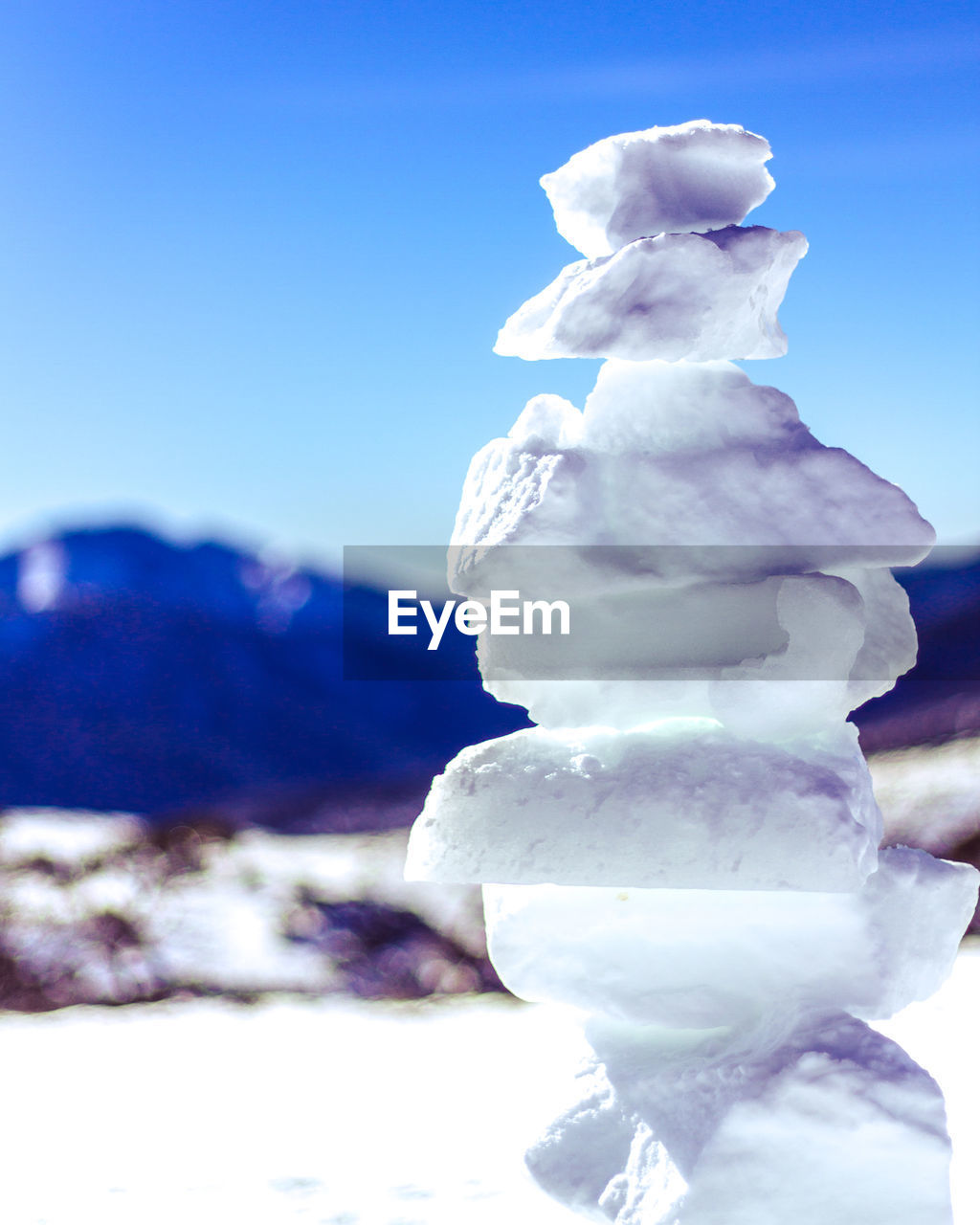 Close-up of snow covered stack against blue sky