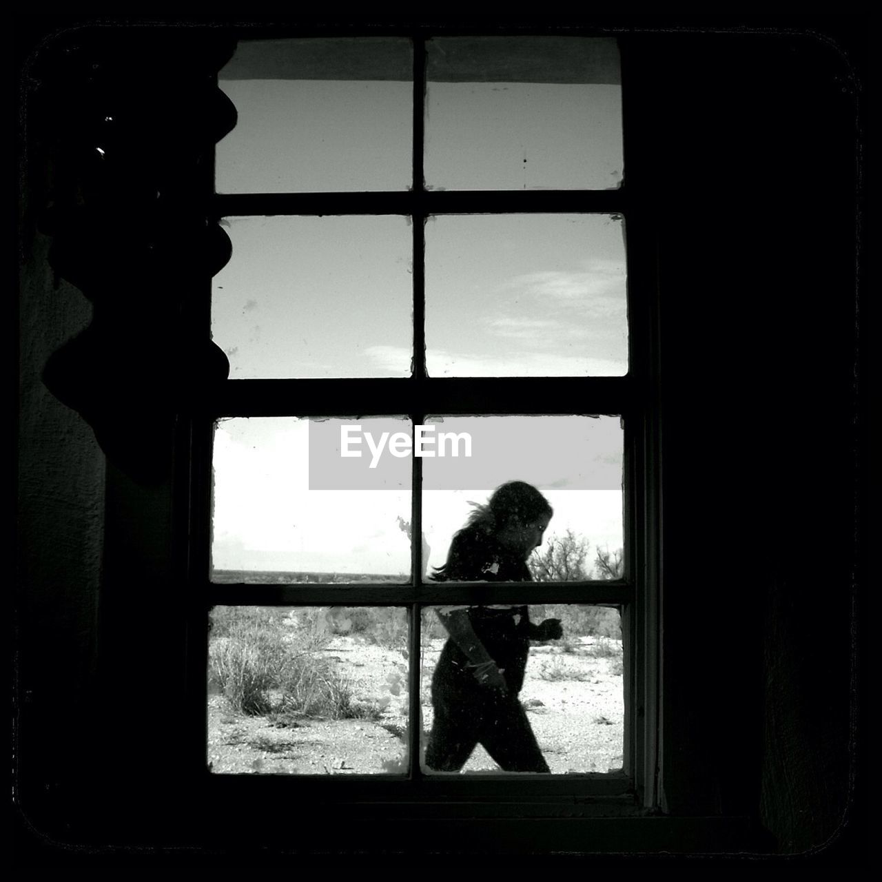 Side view of woman running on field against sky seen through window