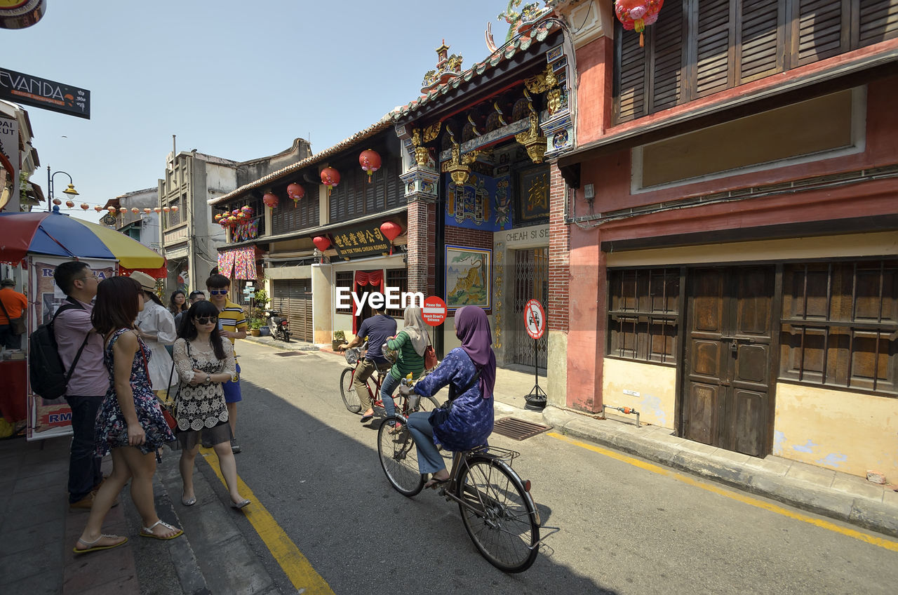 PEOPLE RIDING BICYCLE ON ROAD AGAINST BUILDINGS