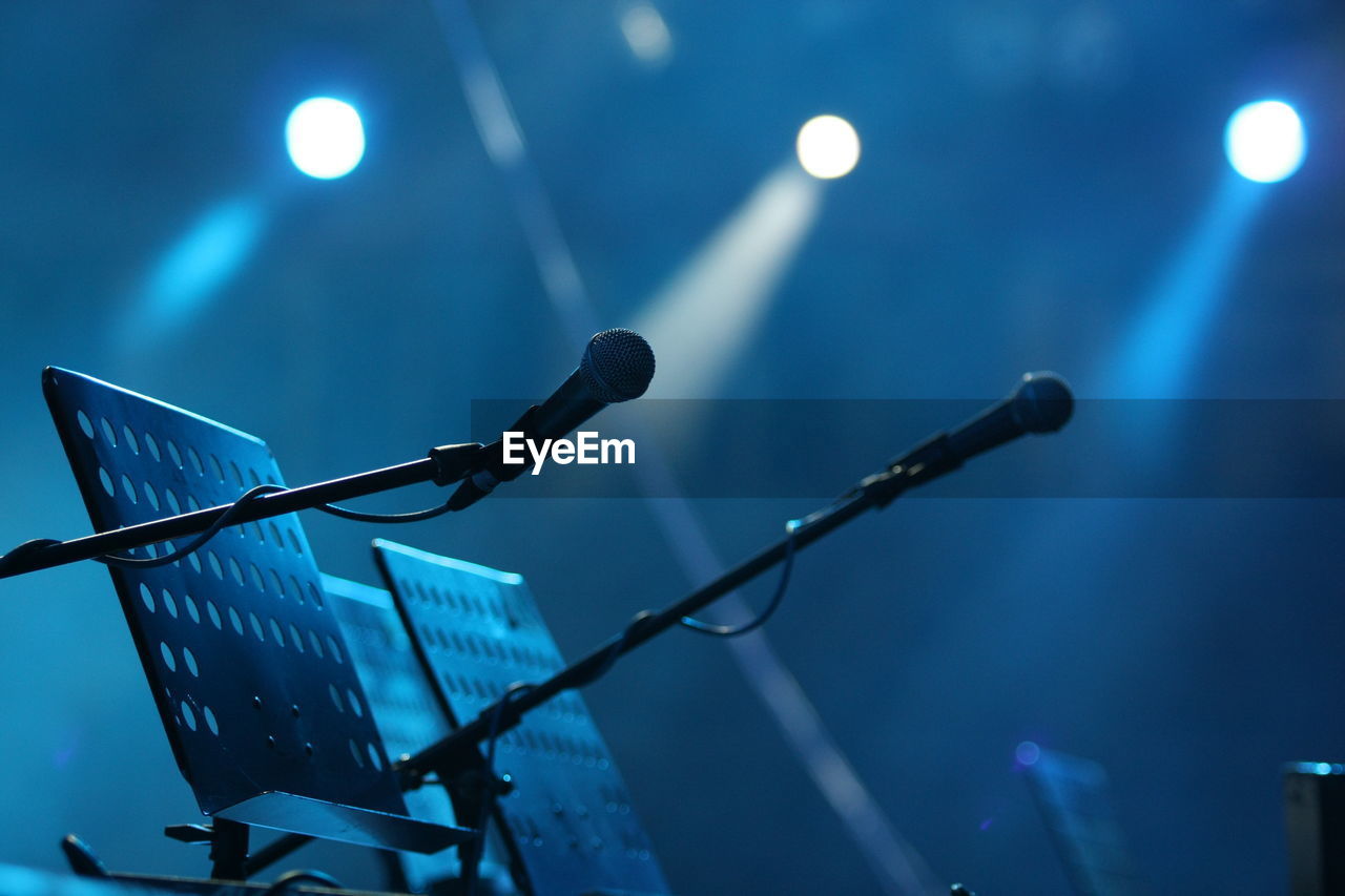 Close-up of microphone stands against spotlights