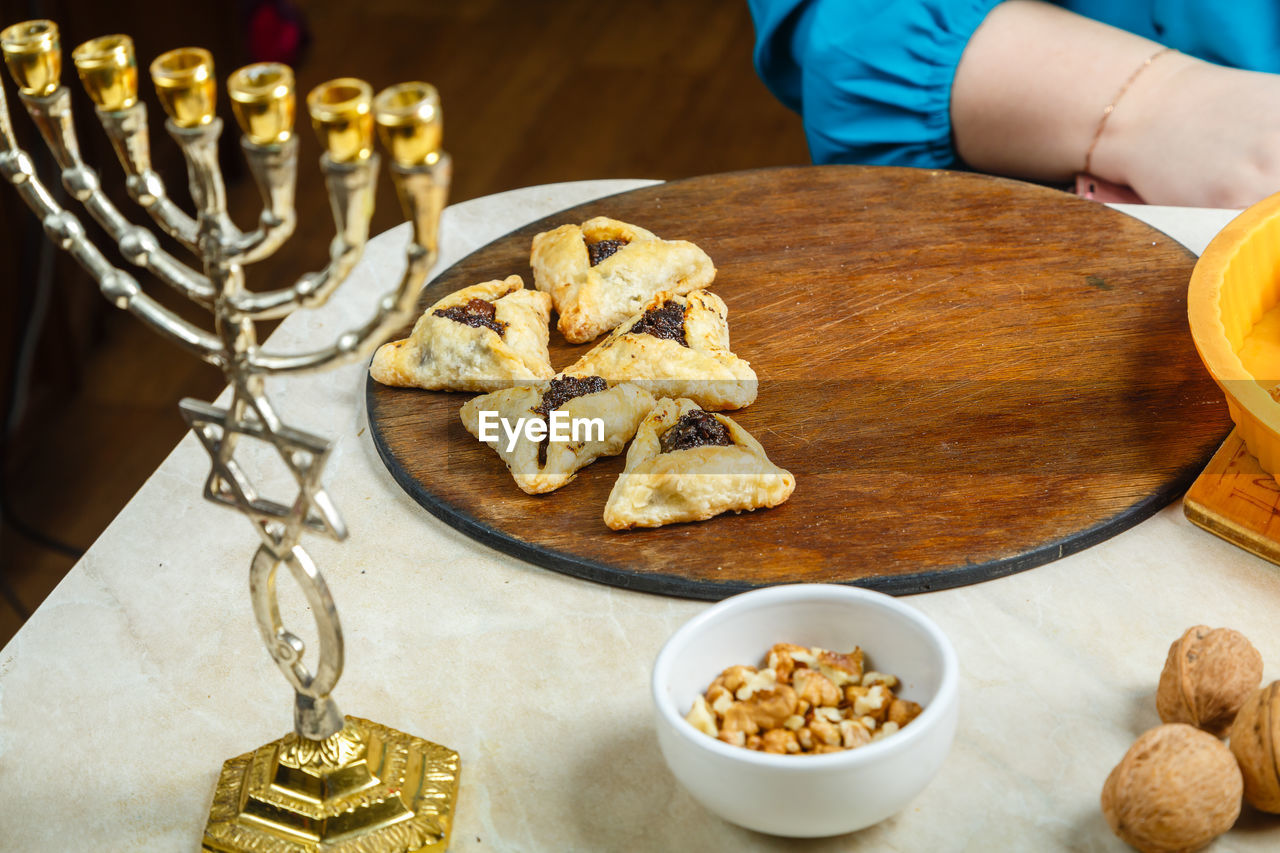 Women's hands laying gomentashi cookies on a wooden board for the festive table for purim.