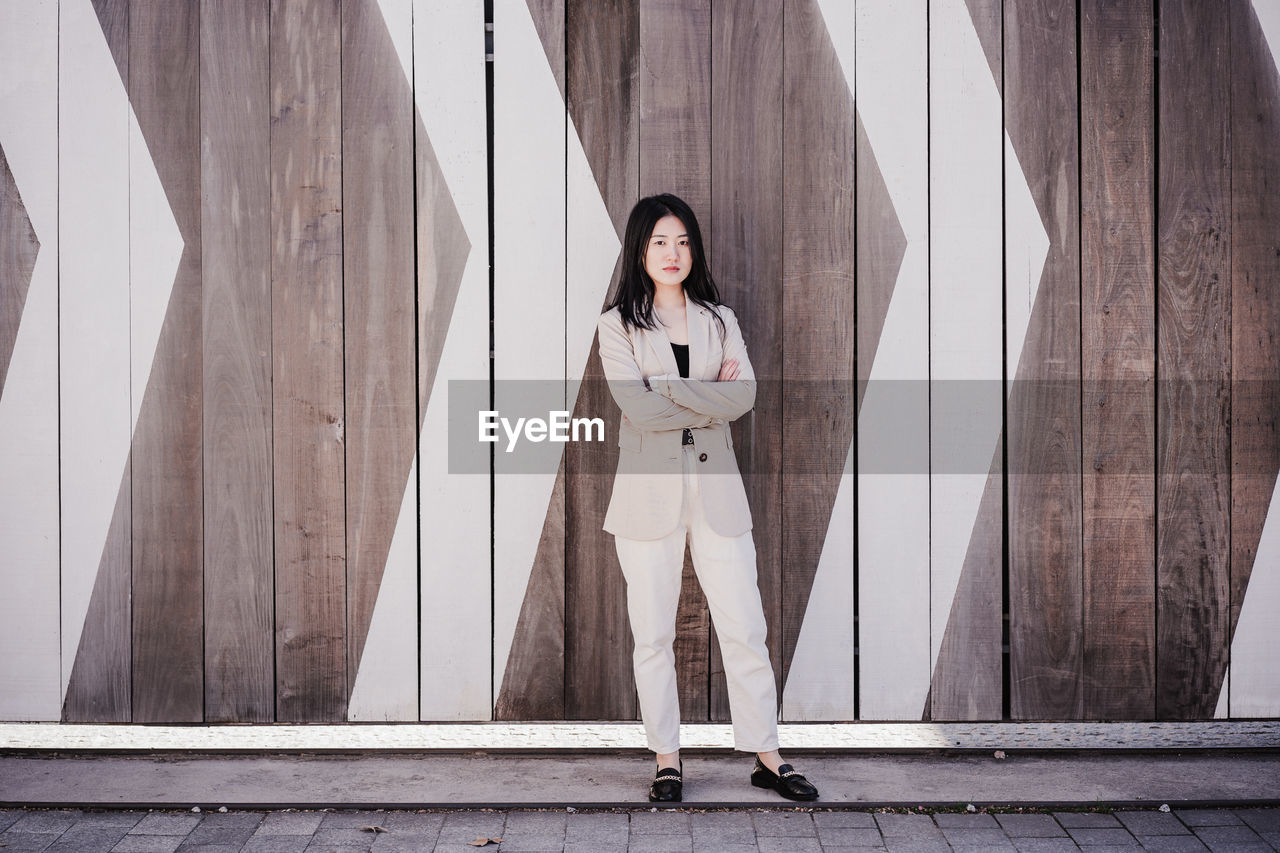 Confident beautiful chinese business woman with arms crossed standing over wood signs background