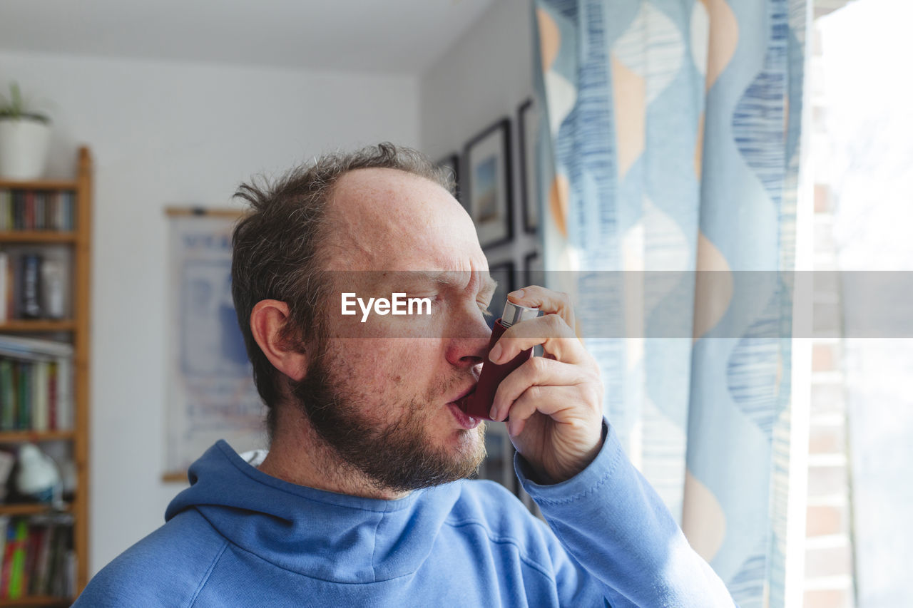 Man with eyes closed using asthma inhaler at home
