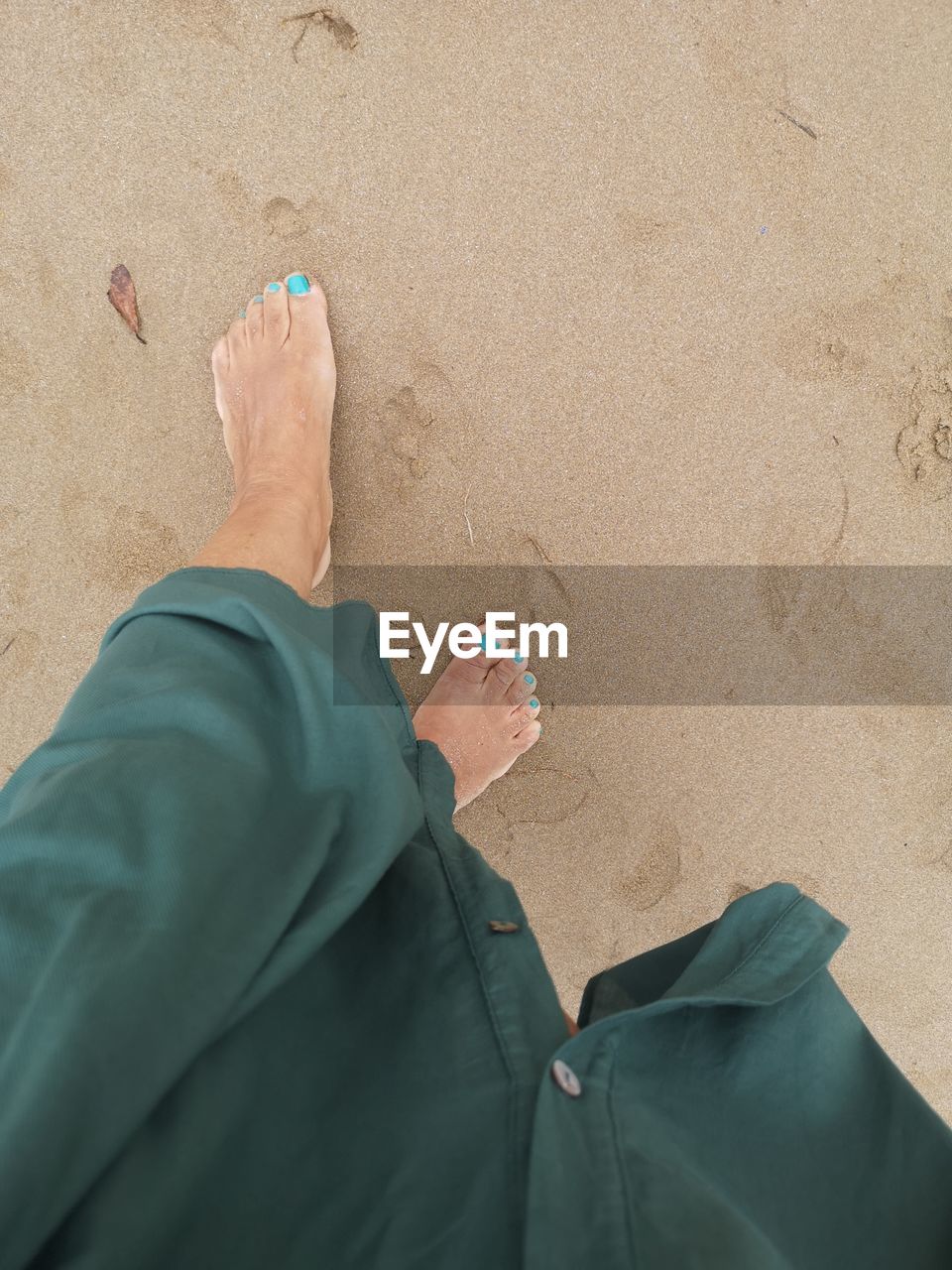 LOW SECTION OF MAN STANDING ON SAND AT BEACH