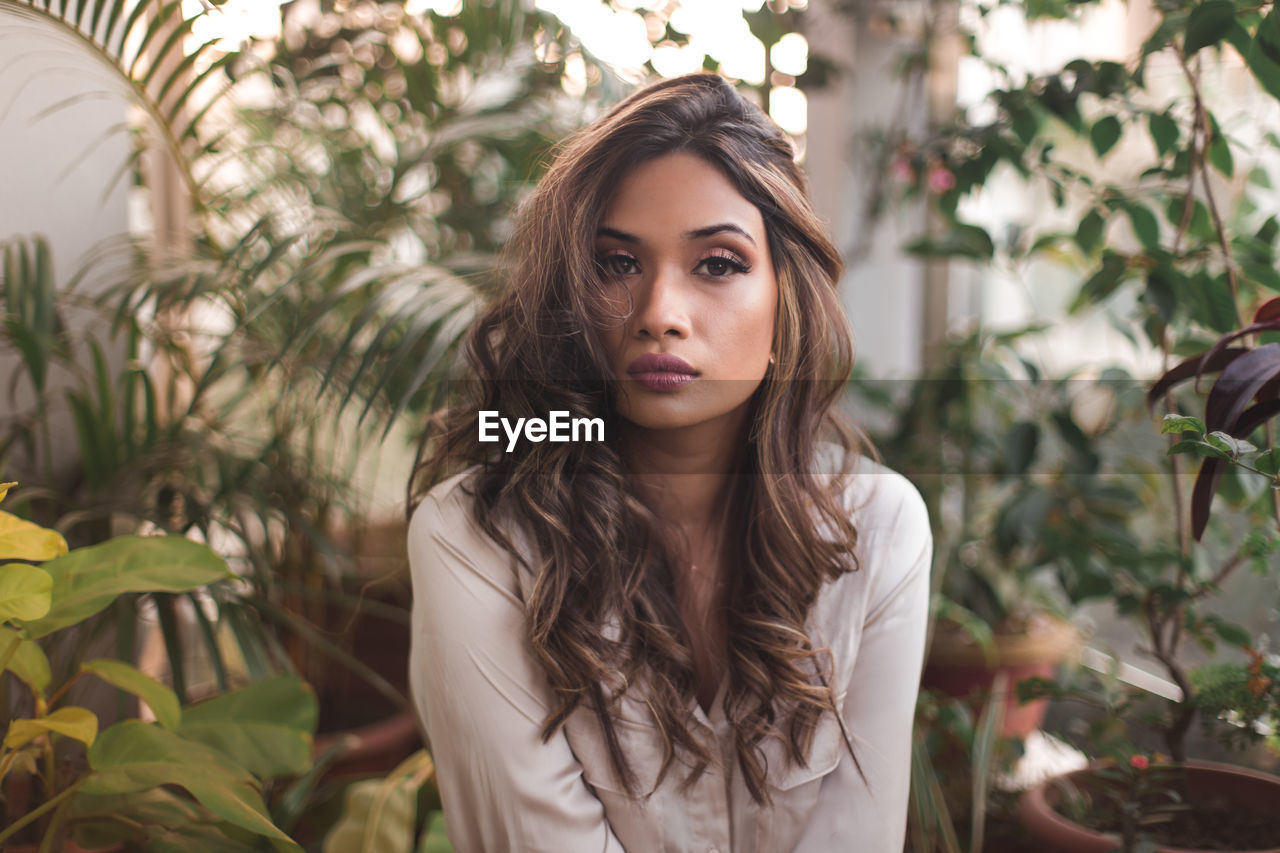 Portrait of beautiful young woman standing against plants