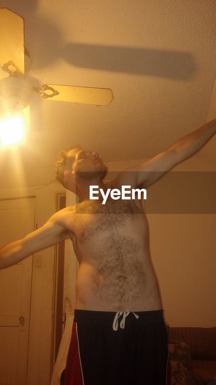 Shirtless man standing with arms outstretched in illuminated room