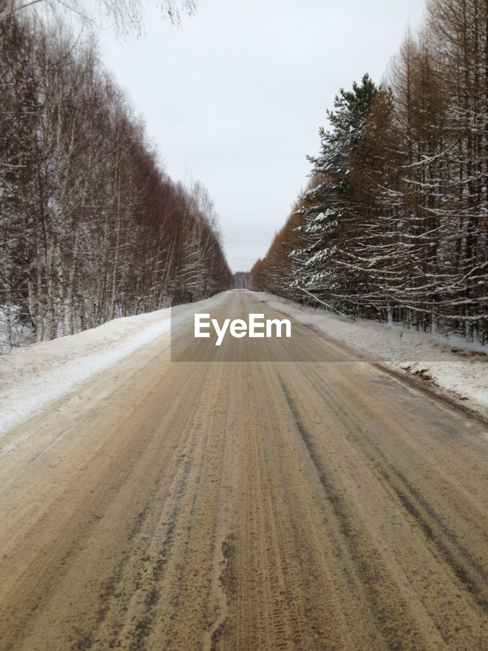 Dirt road amidst snow covered land against sky