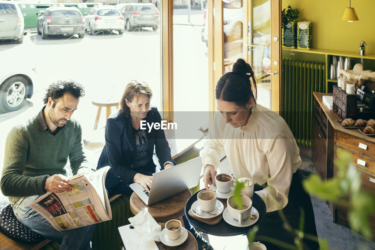 High angle view of waitress picking up coffee cups while customers sitting at table