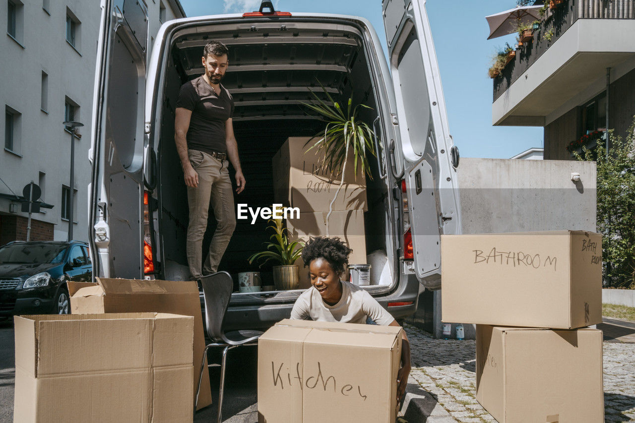 Smiling woman arranging boxes with boyfriend standing in van trunk