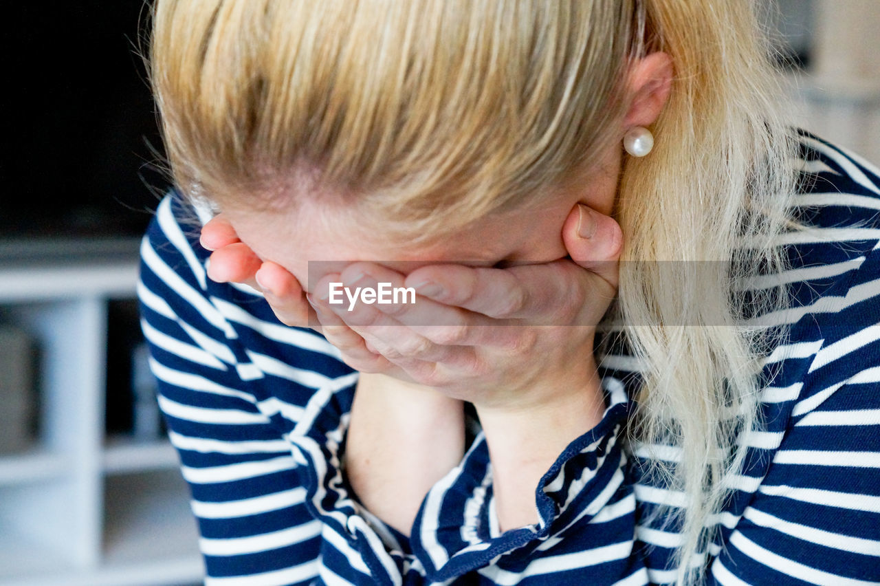 Close-up of depressed woman covering face with hands at home