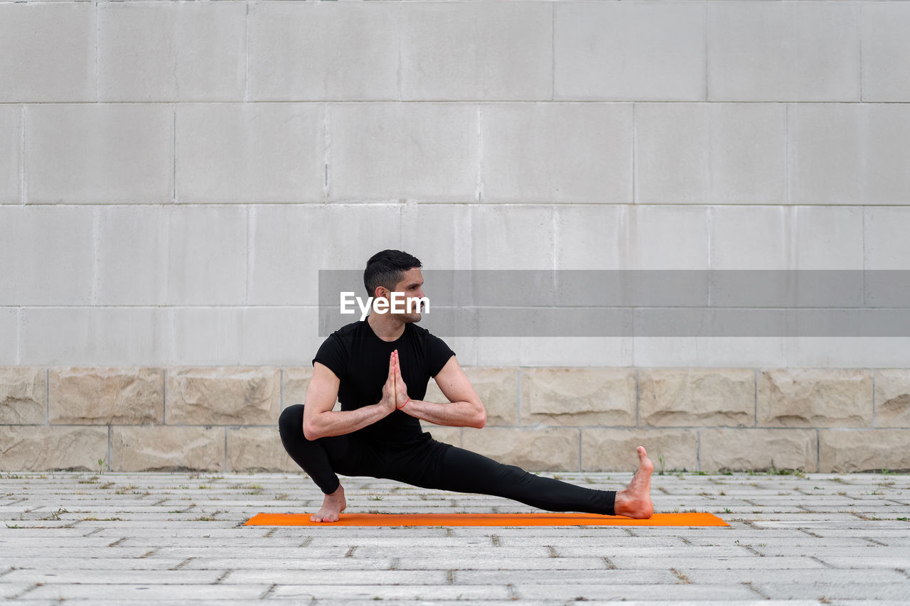 Full length of man exercising on street against wall