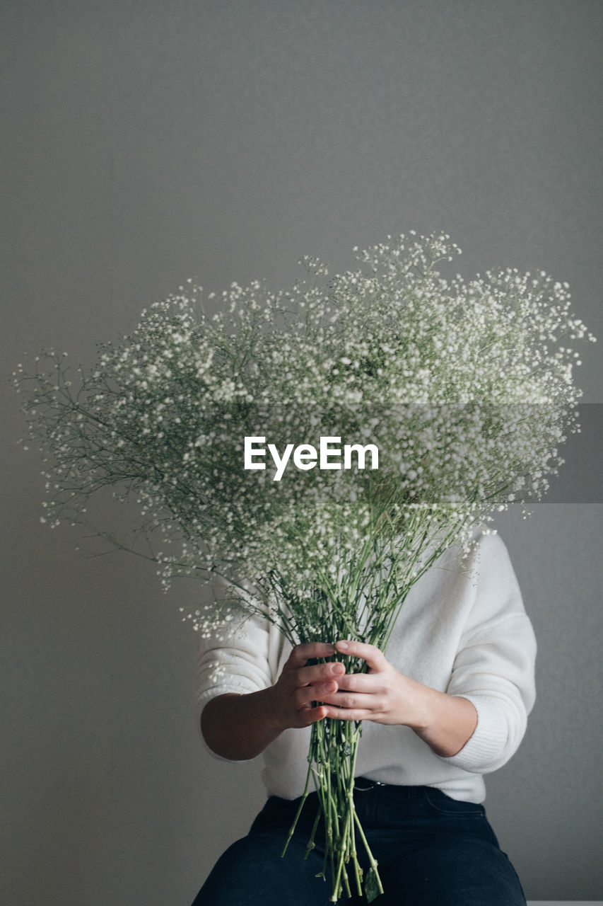 Woman holding white gypsophila blooming flowers, hiding behind bouquet