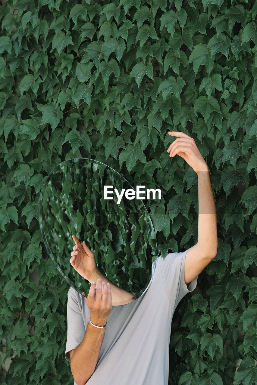 Man holding mirror while standing by plants