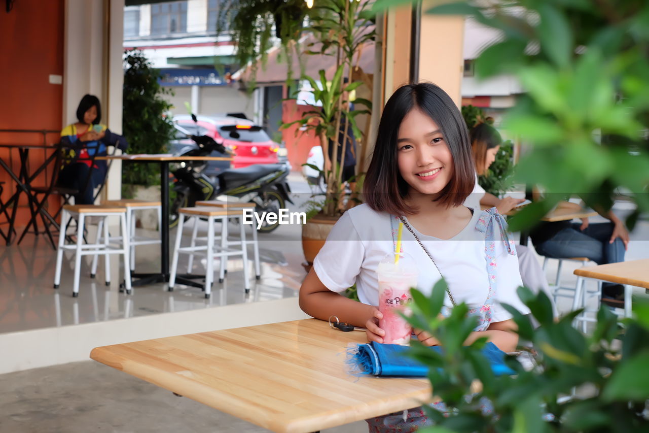 Portrait of smiling young woman sitting at sidewalk cafe
