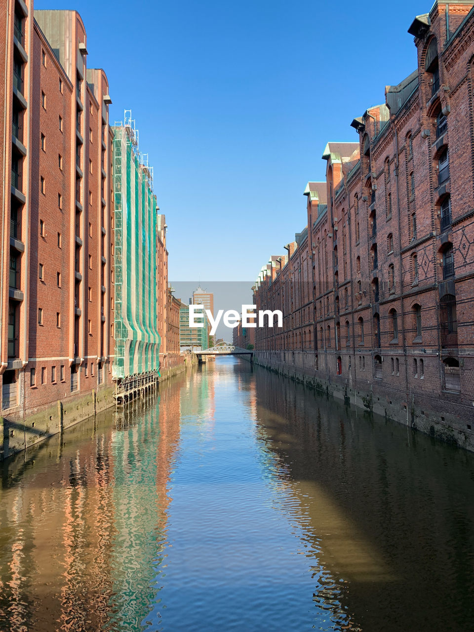 Canal amidst buildings against clear blue sky