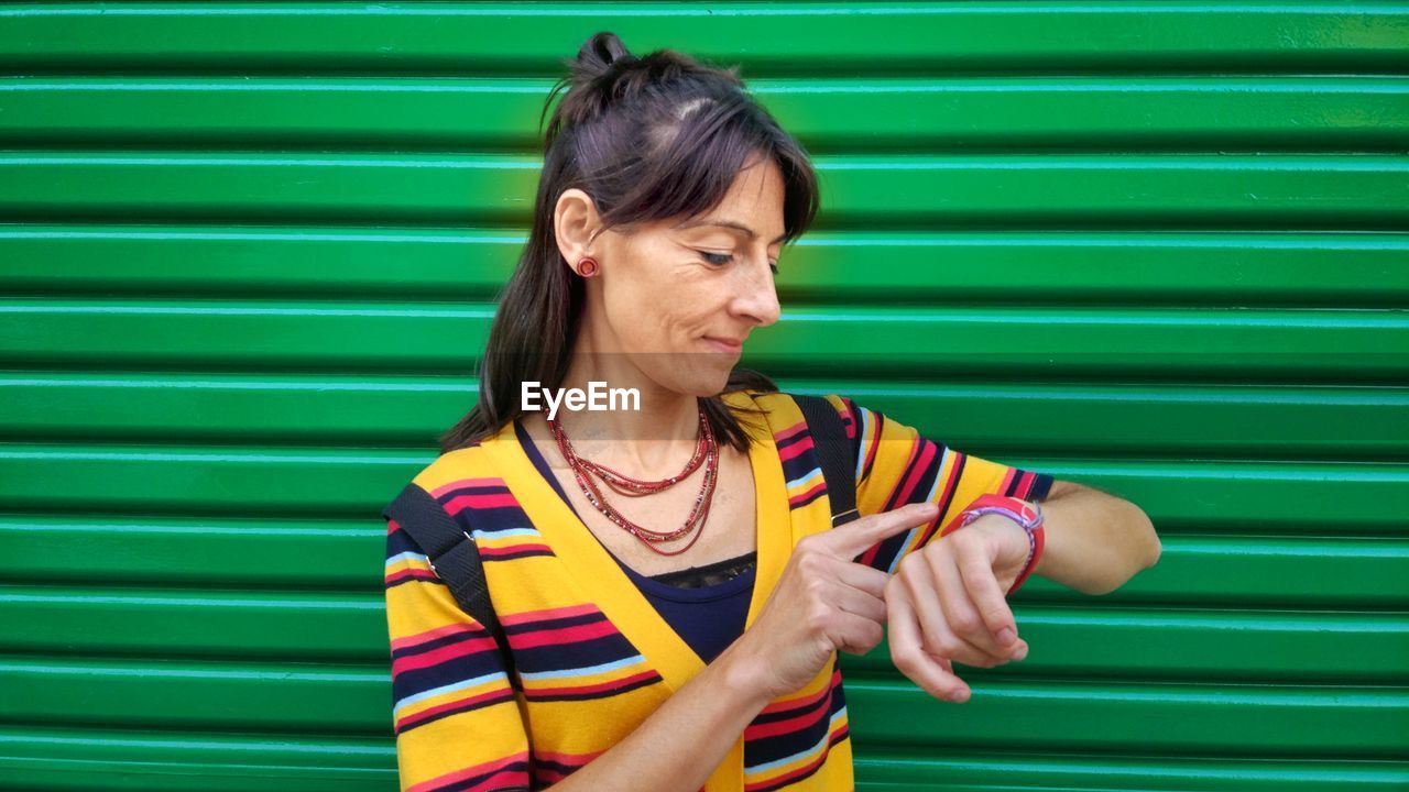 Smiling mature woman checking time against green 