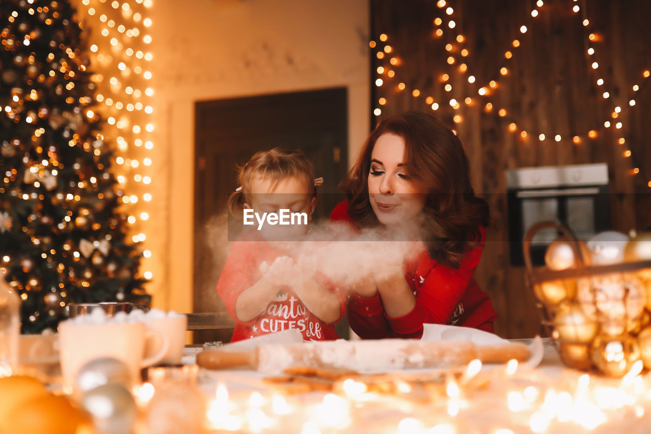 Mom and daughter in are preparing a festive meal in decorated kitchen with a christmas tree at home