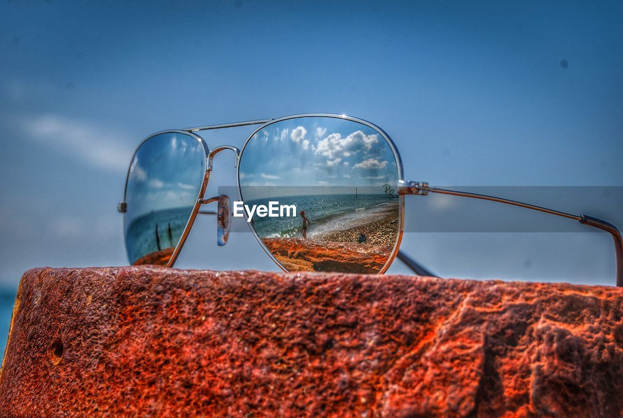 Close-up of sunglasses on rock with beach reflections