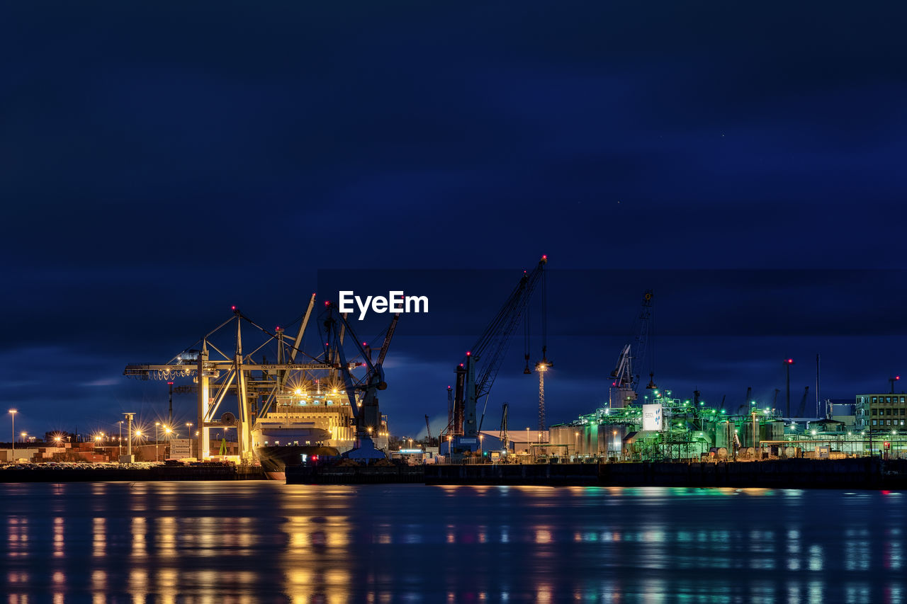 Illuminated factory against cloudy sky at night