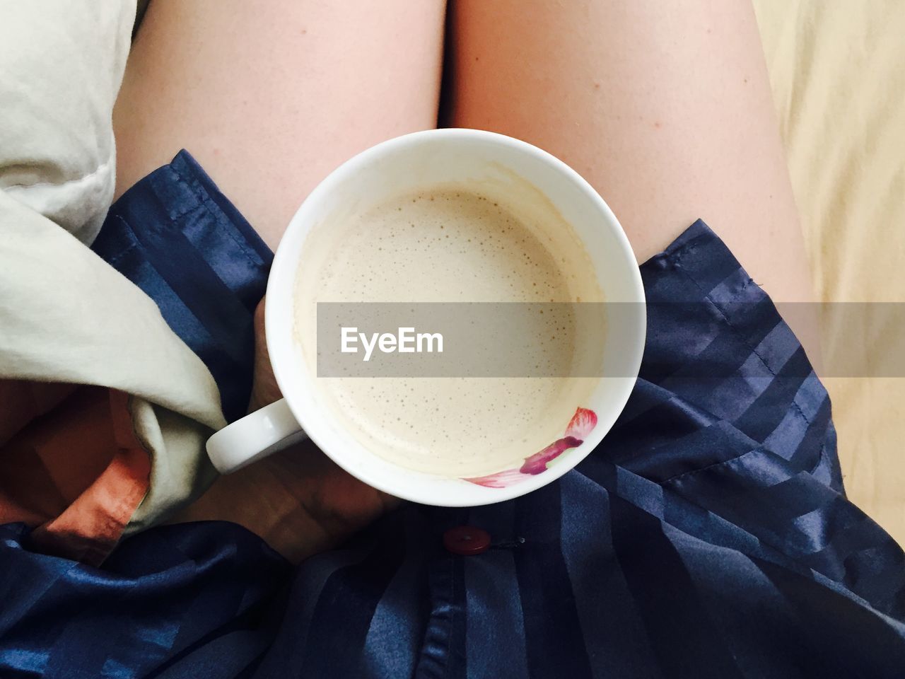 Low section of woman holding coffee cup on bed