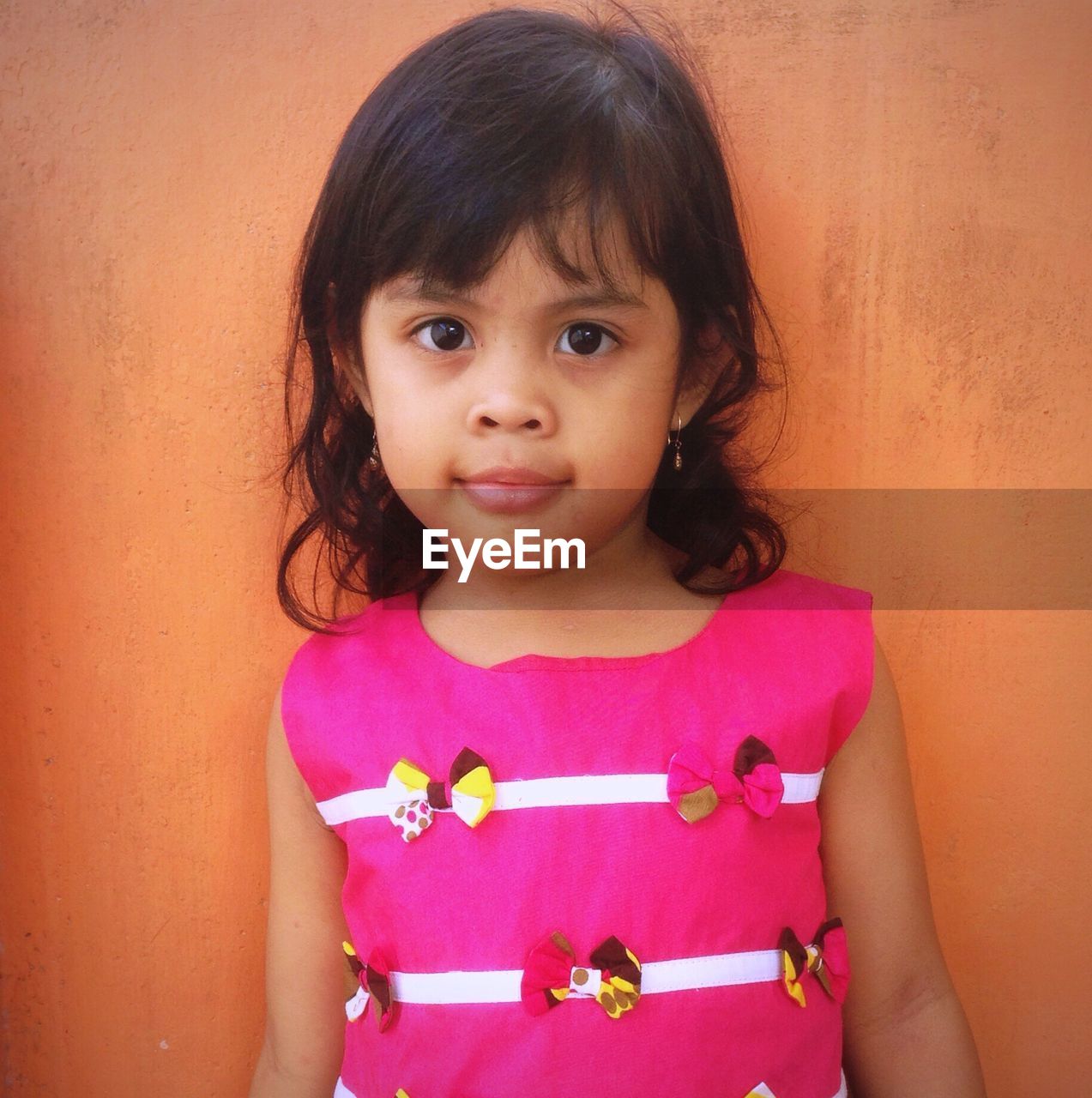 Close-up portrait of girl standing against brown wall