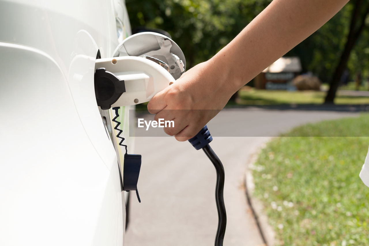 Cropped hand charging car at station