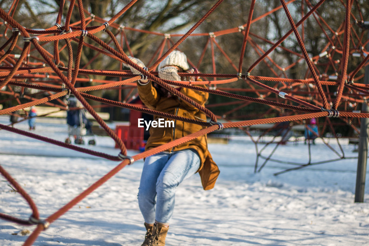 Full length of woman climbing on ropes at snow covered park