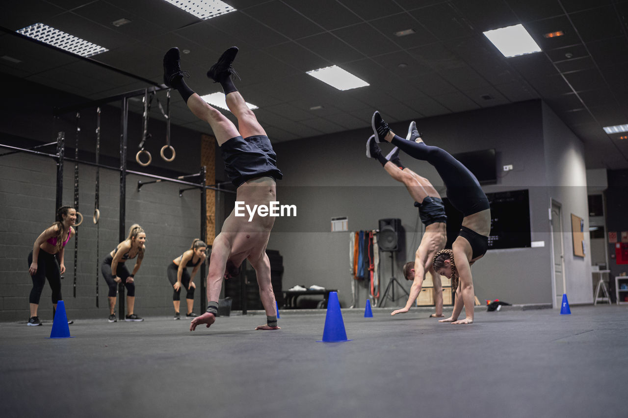 Athletes walking on hand with women motivating in background at gym