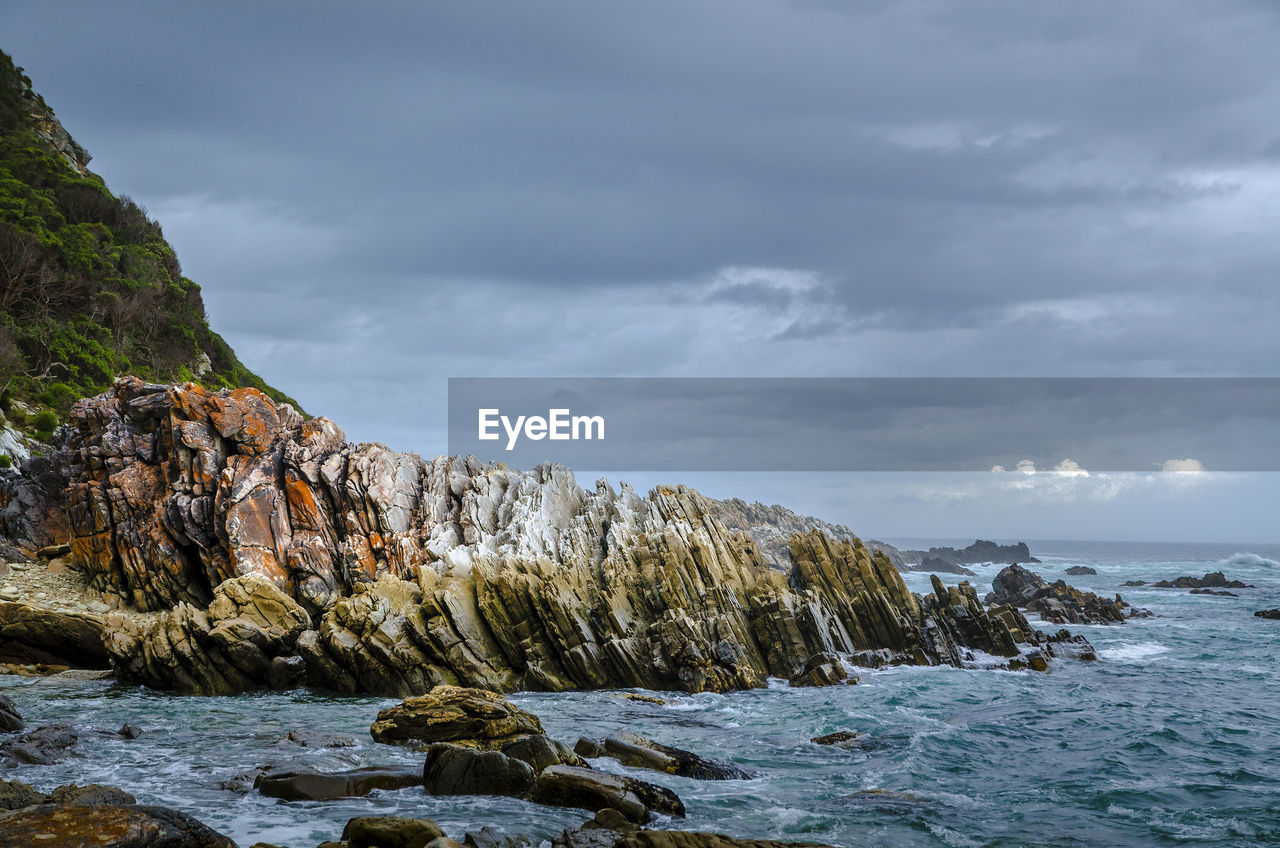 Scenic view of sea and rocky mountains against cloudy sky