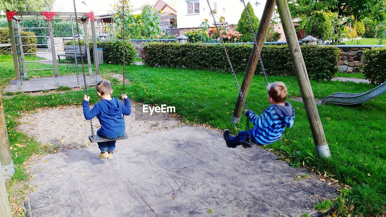 Boys swinging at park against houses