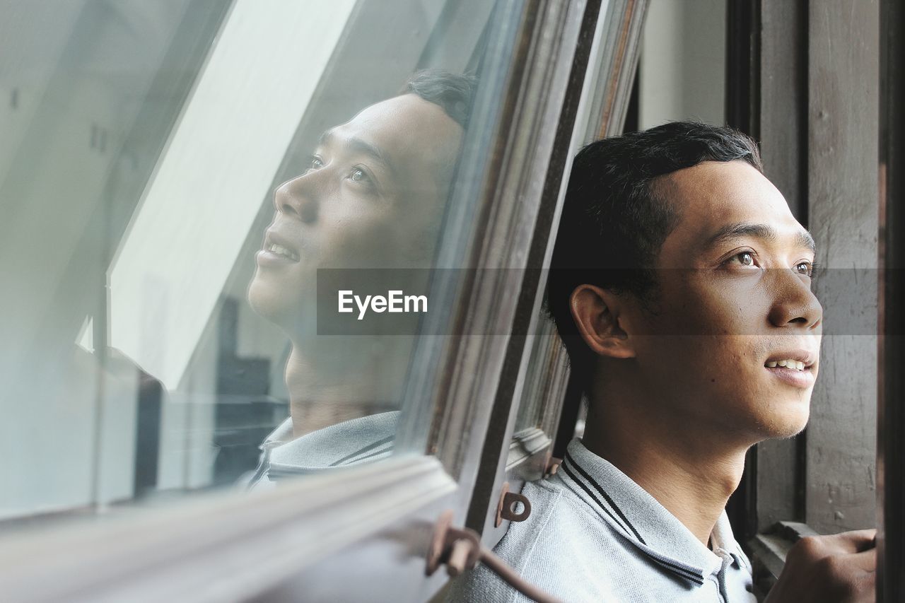 Close-up of smiling young man looking away against window