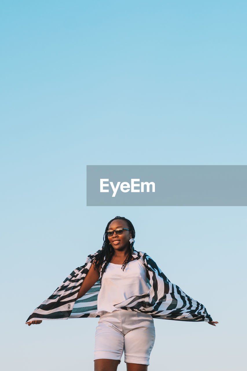 Portrait of young woman standing against clear sky